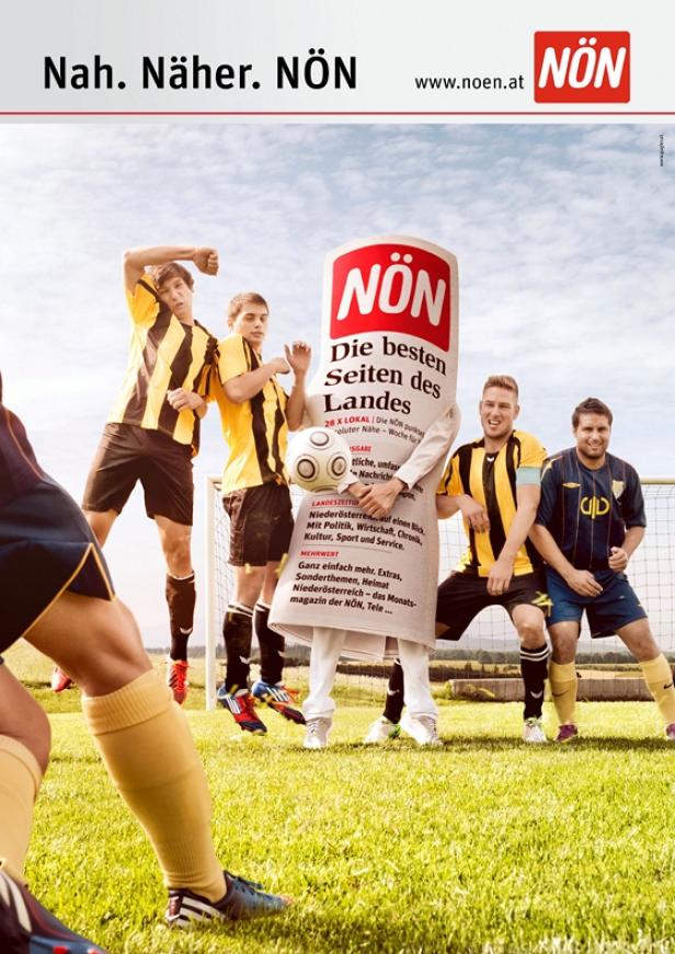 Eine Person im NÖN-Kostüm steht mit einer Gruppe von Fußballspielern auf einem Fußballfeld.