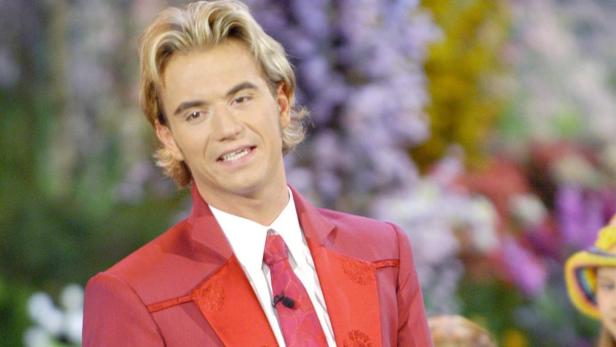 Ein Mann mit blonden Haaren und rotem Anzug lächelt in die Kamera.