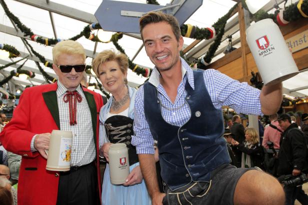 Drei Personen in Tracht posieren mit Bierkrügen auf dem Oktoberfest.