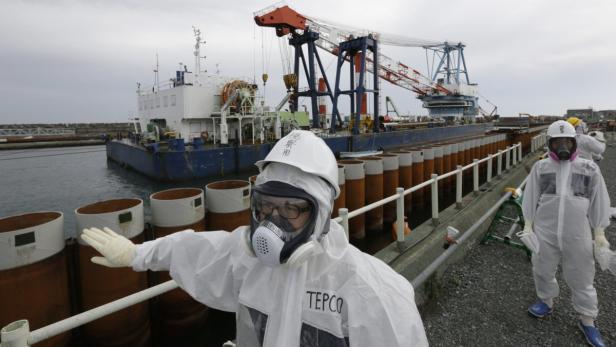 Zwei Arbeiter in Schutzanzügen und mit Atemschutzmasken stehen vor einem Schiff mit einem Kran.