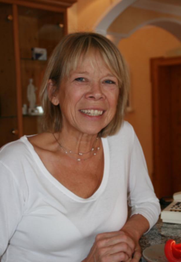 Eine lächelnde Frau mit blonden Haaren und einem weißen Oberteil.