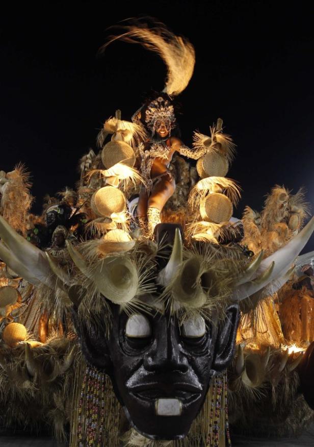 Eine Tänzerin in einem aufwendigen Kostüm auf einem Karnevalswagen mit einer großen Maske.