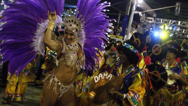 Eine Tänzerin mit lila Federn und ein Schlagzeuger treten bei einem Karneval auf.