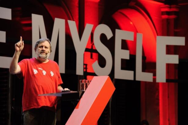 Slavoj Žižek gestikuliert auf einer Bühne vor dem Schriftzug „Myself“.