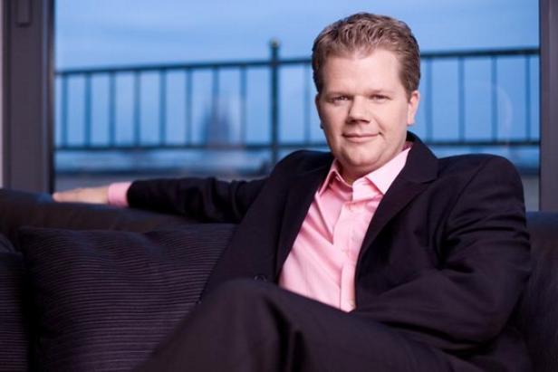 Thilo Burgey, geschäftsführender Gesellschafter von Videovalis, nutzt die SevenOne Media-Vermarktung um das Bewegtbild-Angebot in Österreich auszurollen, zu expandieren und diese Schritte aus dem Potenzial des Marktes heraus zu finanzieren (c: bbg) Ein Mann in einem rosa Hemd und einem dunklen Anzug sitzt auf einem Sofa.