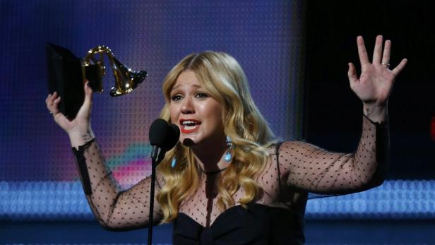 Kelly Clarkson hält eine Trophäe in die Höhe und gestikuliert mit der anderen Hand.