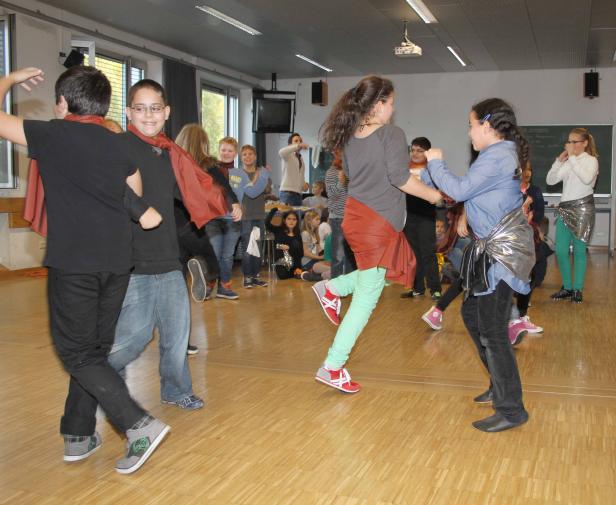 Eine Gruppe von Kindern tanzt in einer Turnhalle, einige tragen Kostüme.