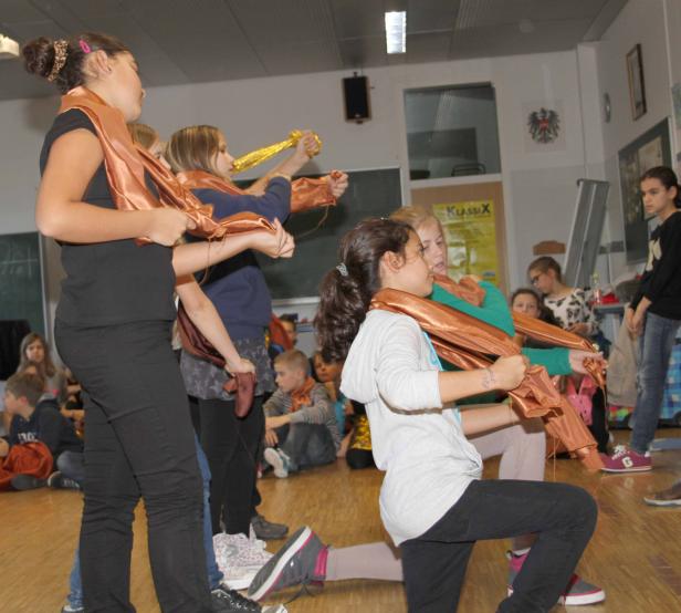 Eine Gruppe von Kindern führt mit bronzefarbenen Tüchern eine Performance auf.