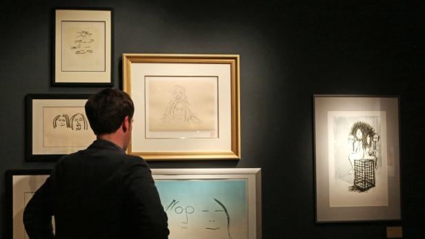 Ein Mann betrachtet eine Ausstellung mit Zeichnungen an einer dunklen Wand.