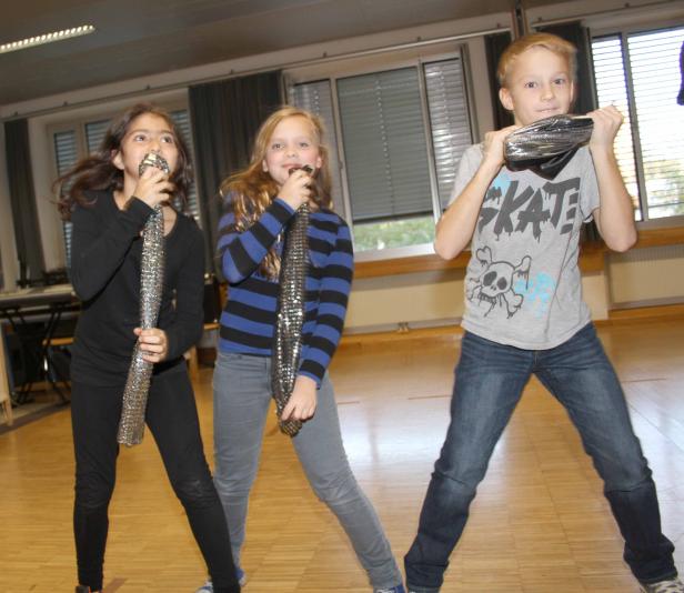 Drei Kinder singen mit glitzernden Mikrofonen in einem Raum.