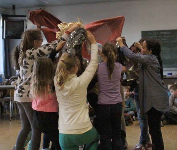 Eine Gruppe von Kindern hantiert mit glänzenden Stoffen in einem Raum.