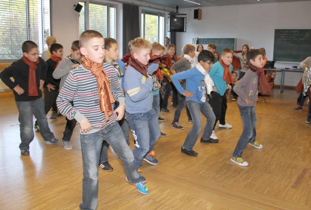 Eine Gruppe von Jungen tanzt in einem Klassenzimmer mit bunten Tüchern.