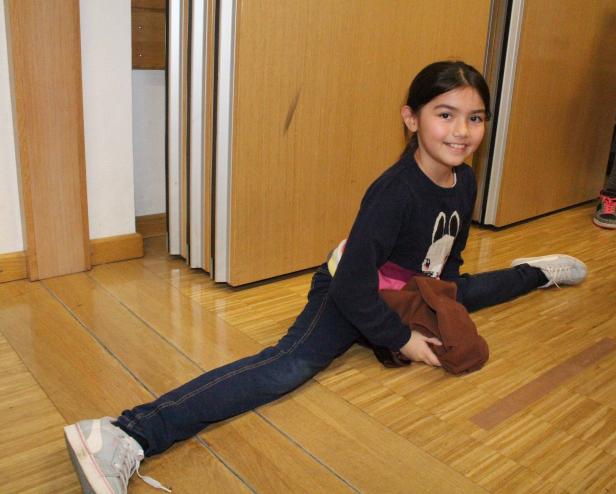 Ein junges Mädchen macht den Spagat auf einem Holzboden.