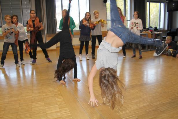 Zwei Mädchen machen Handstände vor einer Gruppe von Kindern in einem Raum.