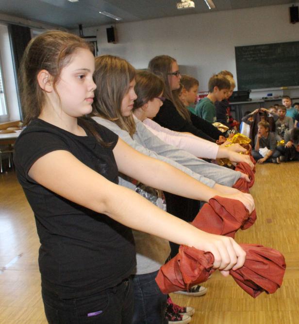 Eine Gruppe Schülerinnen hält rote Tücher in einer Reihe, während andere Kinder zuschauen.