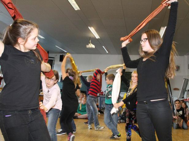Eine Gruppe von Kindern tanzt mit bunten Tüchern in einem Raum.