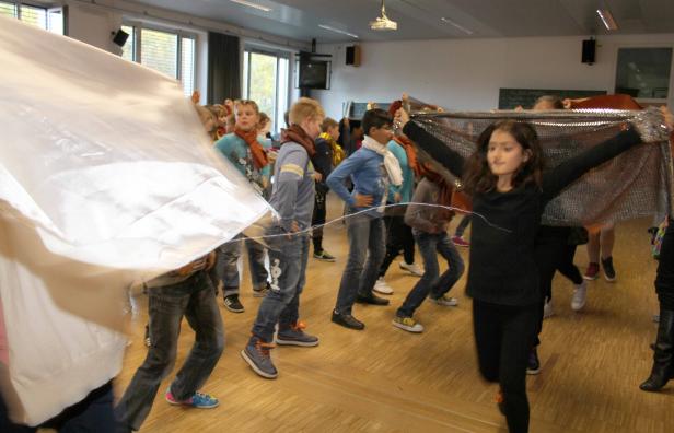 Eine Gruppe von Kindern bewegt sich mit Tüchern in einem Raum.