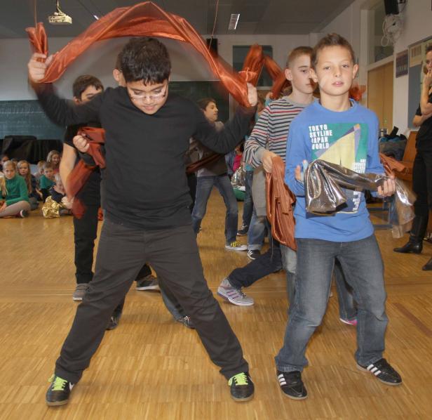 Eine Gruppe von Kindern führt mit Tüchern eine Performance auf einer Bühne auf.