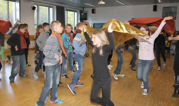 Eine Gruppe von Kindern tanzt mit Tüchern in einem Raum.