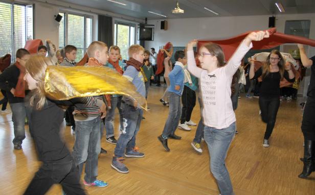 Eine Gruppe von Kindern tanzt mit bunten Tüchern in einem Raum.