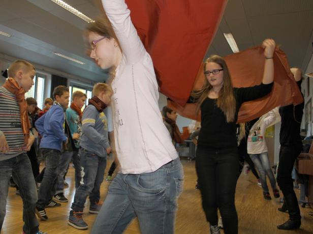 Eine Gruppe von Jugendlichen tanzt mit einem großen, roten Tuch in einem Raum.