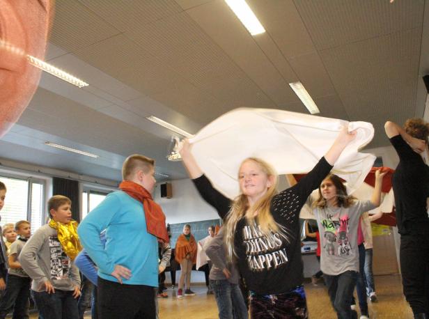 Eine Gruppe von Kindern führt in einem hellen Raum ein Theaterstück auf.