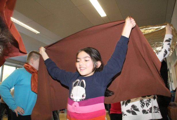 Ein junges Mädchen hält mit anderen Personen ein großes, braunes Tuch hoch.