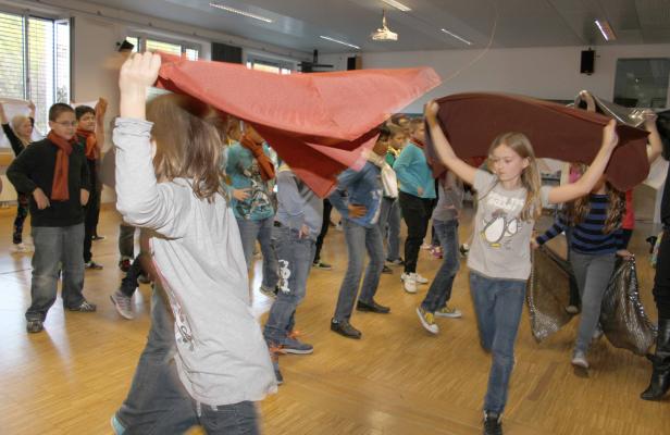 Eine Gruppe von Kindern tanzt mit Tüchern in einer Turnhalle.
