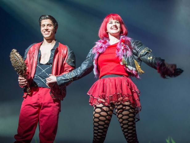 Zwei Darsteller in farbenfrohen Kostümen stehen auf einer Bühne.