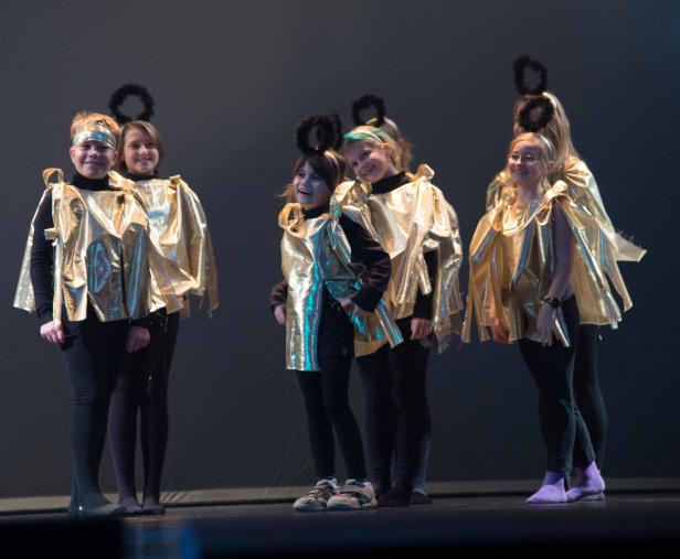 Eine Gruppe Kinder in goldenen Kostümen und mit Heiligenscheinen auf einer Bühne.