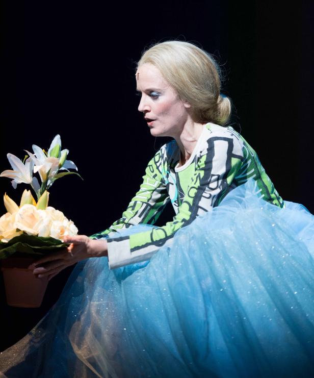 Eine Frau im blauen Tüllrock betrachtet einen Topf mit Rosen und Lilien.