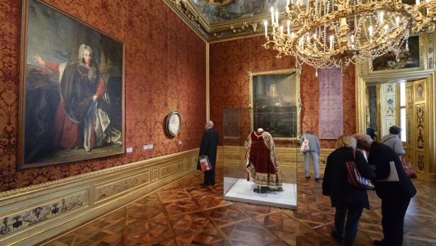 Besucher betrachten Gemälde und eine Robe in einem reich verzierten Raum.