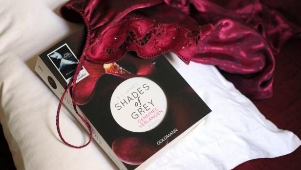 Das Buch „Shades of Grey“ liegt zusammen mit einem roten Negligé auf einem weißen Kissen.