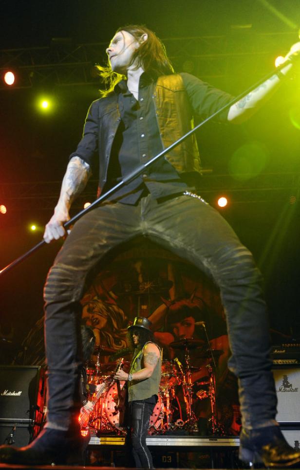 Ein Sänger mit Tätowierungen tritt auf einer Bühne mit einem Mikrofonständer auf.