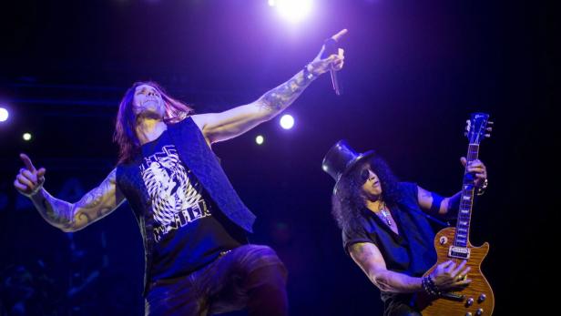 Zwei Musiker, darunter Slash mit Zylinder, treten auf einer Bühne auf.