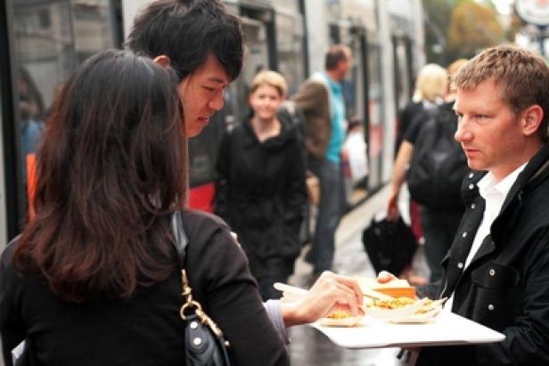 Ein Mann bietet zwei Personen auf der Straße Essen an.