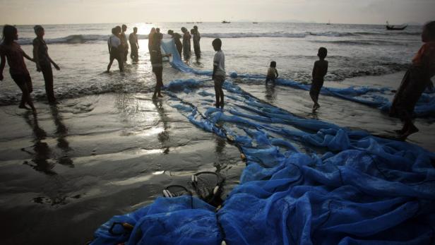 Eine Gruppe von Menschen zieht ein blaues Fischernetz am Strand ins Meer.