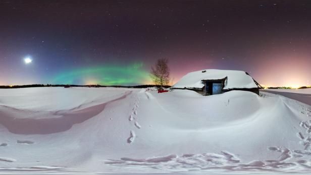 Eine schneebedeckte Hütte unter dem Sternenhimmel mit Nordlichtern.