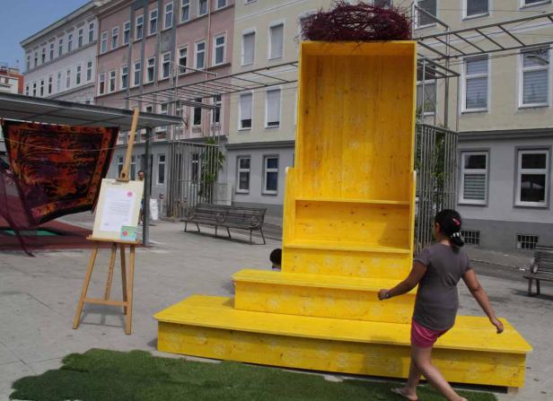 Ein gelbes, treppenartiges Kunstobjekt steht auf einem Platz, während ein Mädchen vorbeigeht.