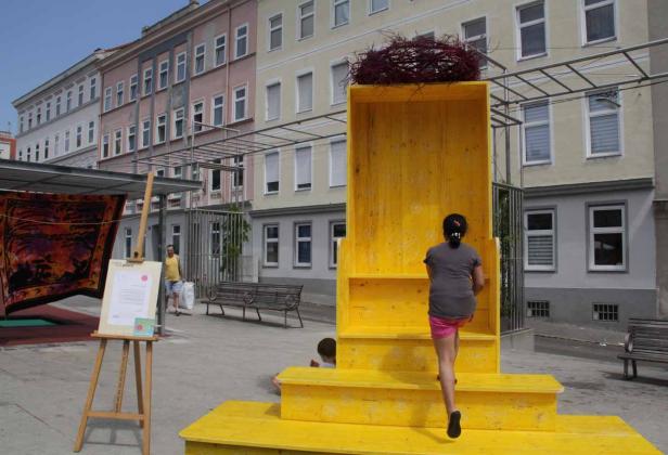 Ein Mädchen steigt auf eine gelbe Installation mit einem Vogelnest oben drauf.