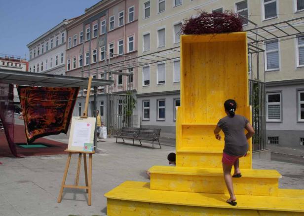 Ein Mädchen klettert auf eine gelbe Installation mit einem großen Vogelnest auf dem Dach.