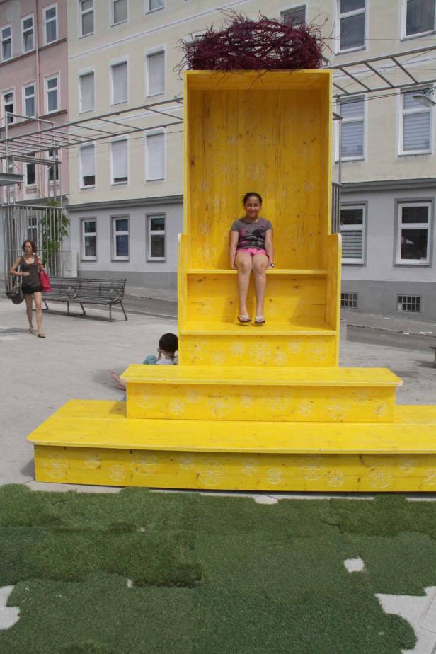 Ein Mädchen sitzt in einer großen, gelben Installation mit einem Nest auf dem Dach.