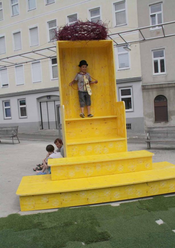 Ein Junge mit Hut steht in einer gelben Installation mit einem Vogelnest oben drauf.