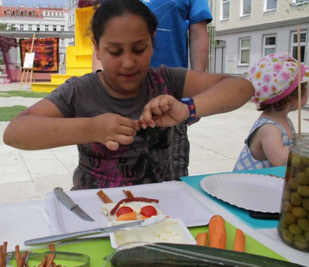 Ein Mädchen bastelt mit Lebensmitteln ein Gesicht auf einem Teller.