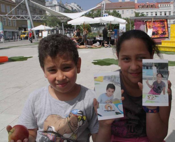 Zwei Kinder halten Fotos von sich auf einem belebten Platz.