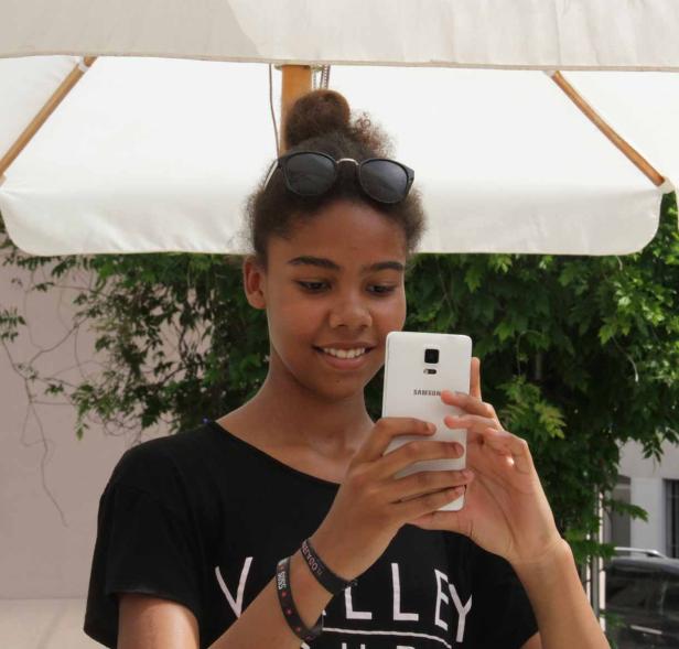 Ein junges Mädchen macht ein Foto mit ihrem Samsung-Smartphone unter einem Sonnenschirm.