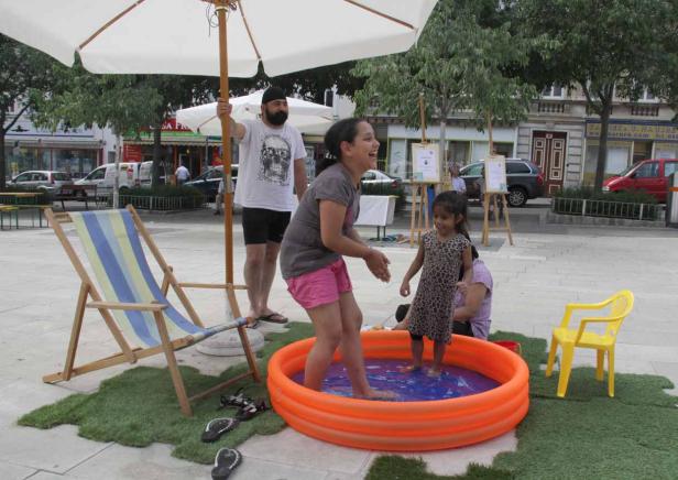 Zwei Mädchen spielen in einem Planschbecken auf einem öffentlichen Platz.