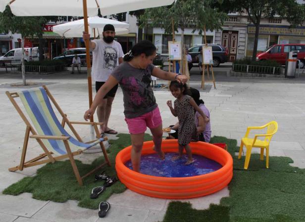 Eine Frau und ein Mädchen stehen in einem Planschbecken auf einem öffentlichen Platz.
