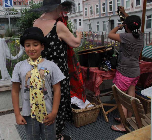 Ein Junge mit Hut und Krawatte steht vor einem Stand mit Kleidung und Accessoires.