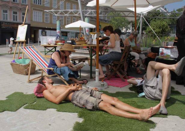 Menschen entspannen sich an einem sonnigen Tag im Freien auf einer Kunstinstallation.